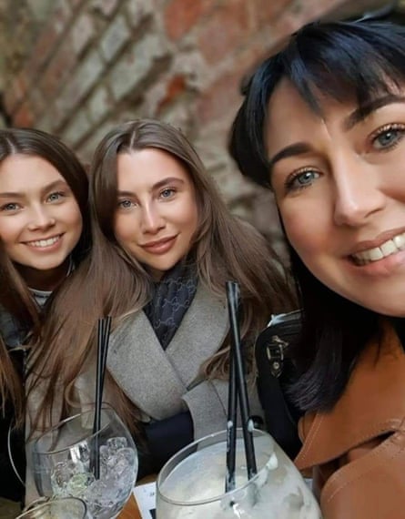 Two young women and their mother hold drinks and smile for the camera.