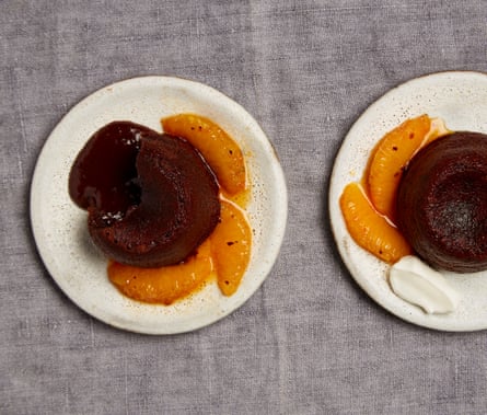 Overhead shot of chocolate pudding oozing with chocolate sauce, and garnished with orange segments, on a white plate. 