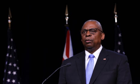 man wearing suit and blue tie stands behind microphone