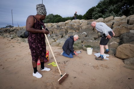 People on a beach with a brush and plastic buckets looking for nurdles