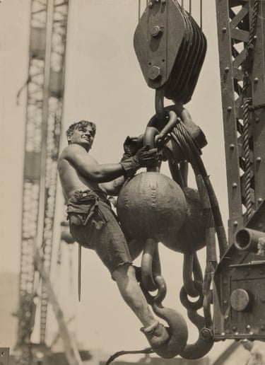 a young man shown in sepia hanging on to huge crane equipment