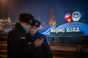 Two policemen check the pictures they have just taken in front of a display with Beijing 2022 Winter Olympics and Paralympics official mascots as they patrol the streets outside of the National Stadium.
