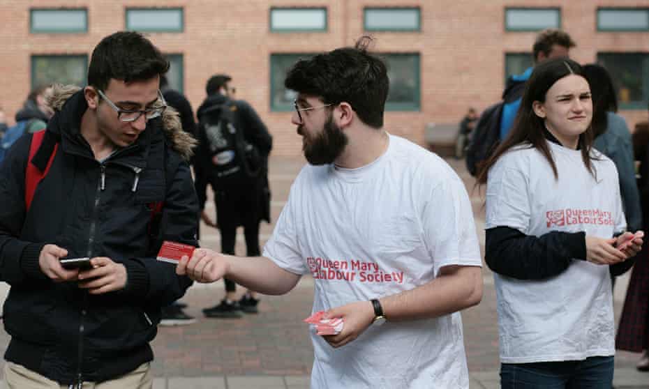 Two people in Labour party T-shirts handing a card to another student