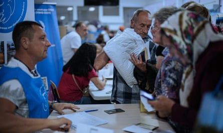 Evacuees lining up at a desk staffed by a man in a blue vest