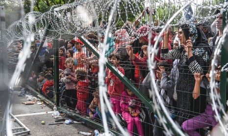 Refugees stand behind a fence at the Hungarian border with Serbia