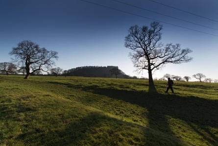 View of a walker on the Sandstone Trail, with Beeston Castle in the background, on a clear winter’s day with long shadows and trees