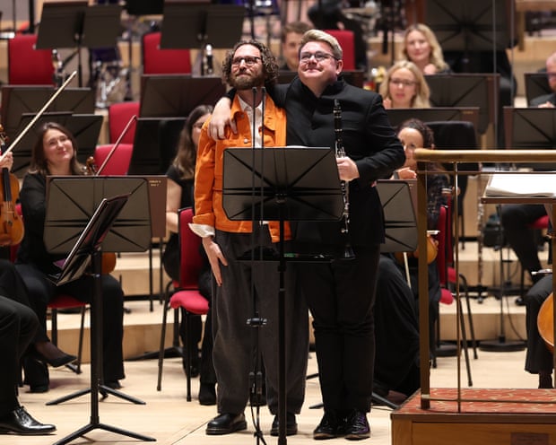 Composer Gavin Higgins and clarinettist Mark Simpson embrace on stage before the orchestra