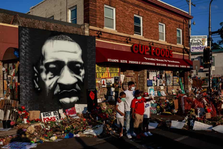 In June, kids pose as their father takes a photo in front of a makeshift memorial to George Floyd near the site where he died in police custody, in Minneapolis.