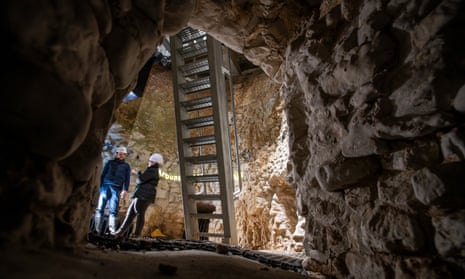 Two people standing next to metal ladder in put below ground