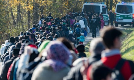 A long line of people are led on foot along a path by German police