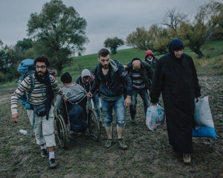 Syrian family carrying a person in wheelchair out of mud