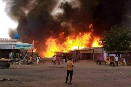 A man in the foreground watches with other people as a huge blaze lights up an area of buildings