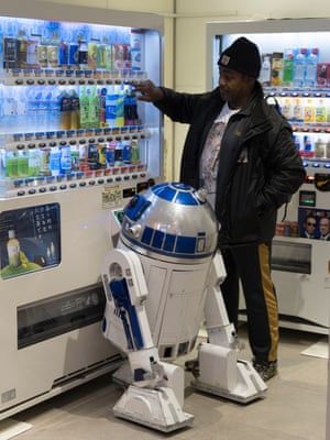 Richard and R2-J1 choose a drink from a vending machine. R2-J1 is moved by remote control, and it beeps, flashes, and swivels its head