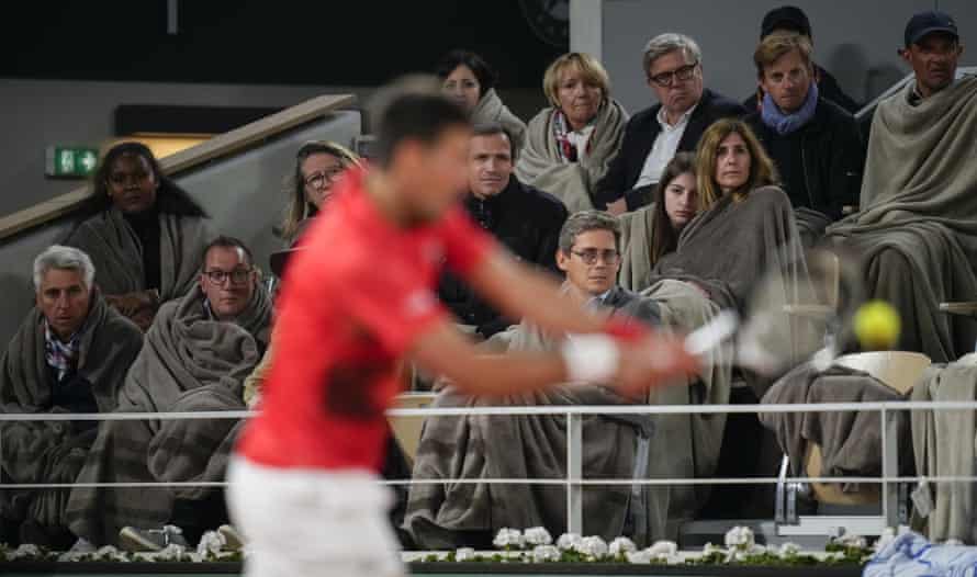 Spectators wrapped in blankets watch as Novak Djokovic plays a shot against Rafael Nadal during their quarter-final match.