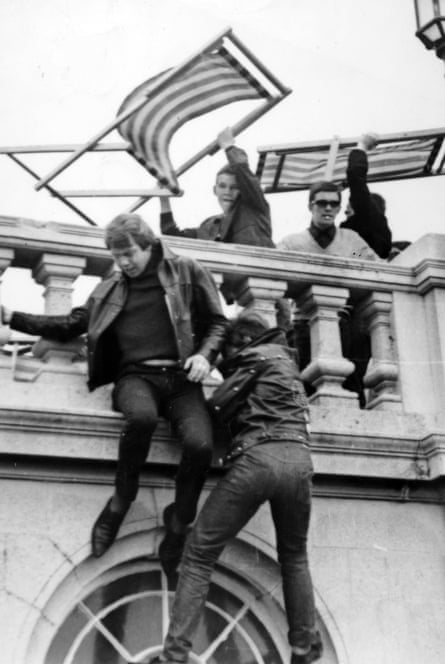 Mods on a rooftop brandish deckchairs as rockers in leather gear try to climb up on the roof