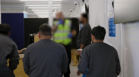 People, with faces blurred, sit on a bench as a man in a hi-vis vest stands in front of them