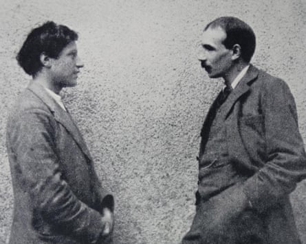 Two men look at each other in front of a wall.