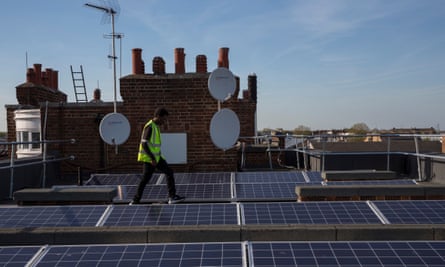 A man walks on a roof between solar panels with chimneys in the background