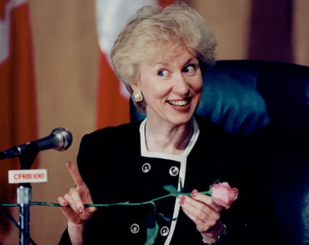 Woman with blond hair and blue jacket holds rose at press conference