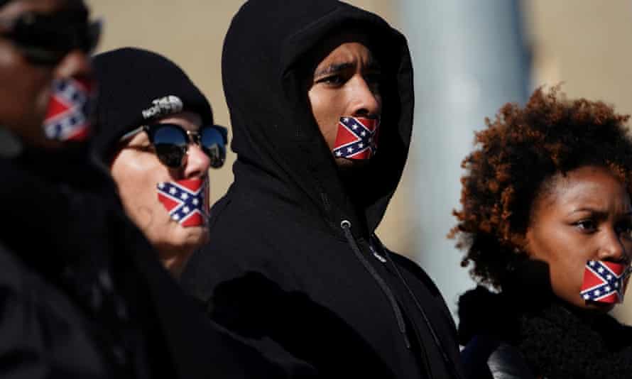 People stand in protest with Confederate flag stickers covering their mouths, outside the museum.