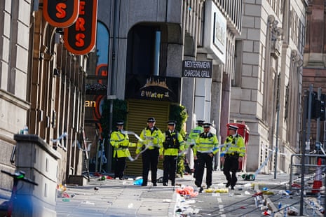Five police officers walk along a road strewn with litter from a victory parade.