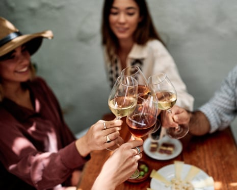 Four hands clink sherry glasses over a table with cheese