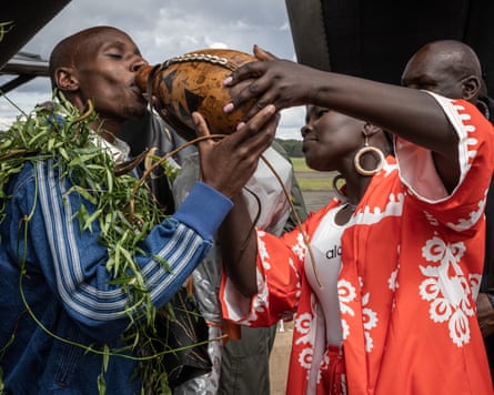 Lydia Sawe helps to tilt a gourd as her husband drinks from it