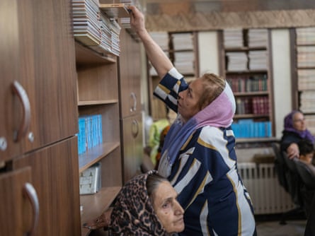 A woman wearing a headscarf reaches up to a shelf