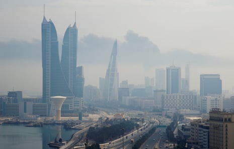 A wide shot of Manama against a grey sky shows smoke clouding visibility.