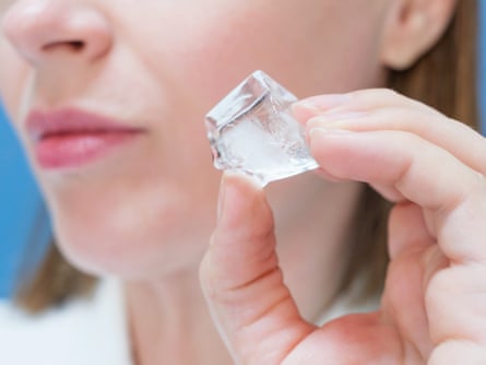 Young woman holding ice cube near her face on blue background