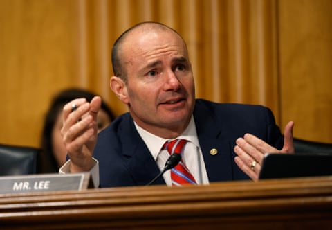 man wearing navy suit and striped red tie gestures while holding pen in hand