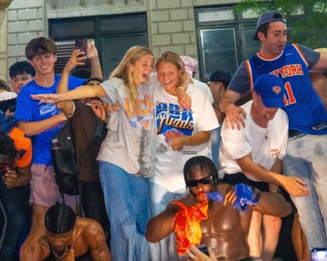 A group of Knicks fans celebrate together on a street, with two women embracing and smiling