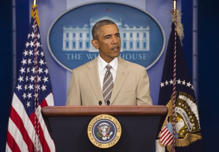Barack Obama speaking at a pedestal wearing a tan suit with striped brown tie