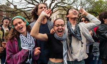 Four young people student in a line with arms up and around each other, wearing keffiyehs and cheering jubilantly.