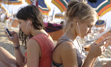 Two teenage girls plugged into mobile phones at the beach
