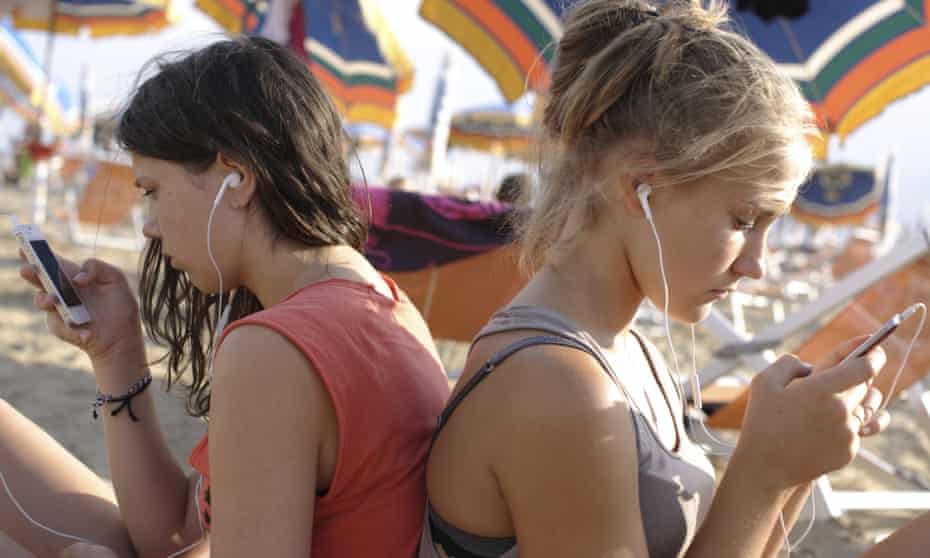 two girls listening to their music on smartphones on the beach