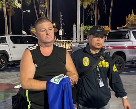 Australian suspect Simon Peter Carman stands beside a uniformed Thai police officer at night