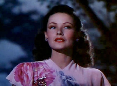 A woman in a pink dress, with dark hair and silver earrings, with a cloudy dark sky behind her