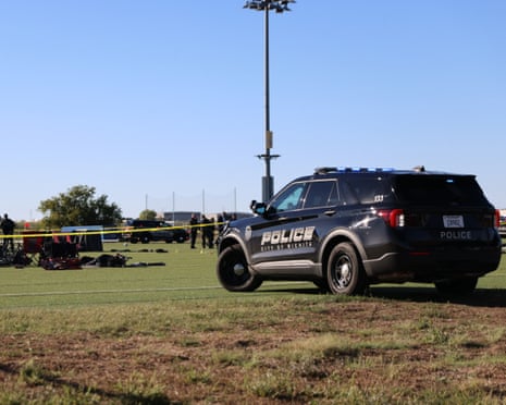 Police SUV parked on grass at soccer field as officials stand on field opposite yellow police tape