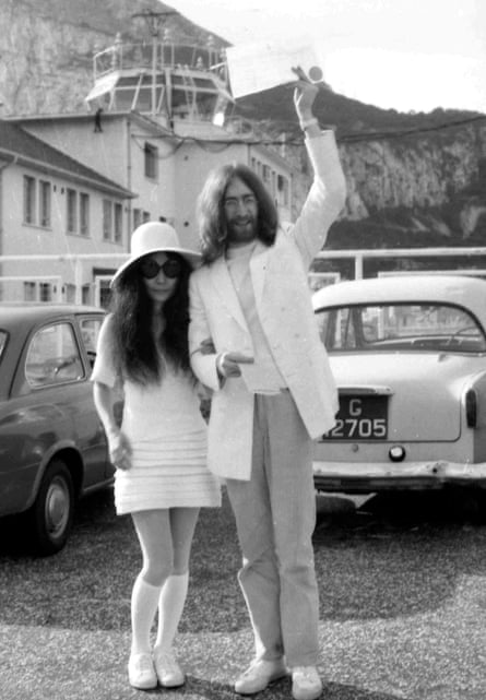 Yoko Ono in white mini dress, hat, sneakers with John Lennon in white jacket waving wedding certifcate in Gibraltar in March 1969.