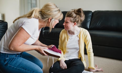 Mother is putting her disabled daughter's shoes on at home.