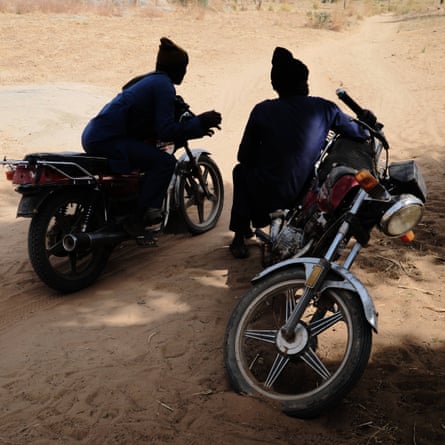 Two gang members sit on their motorcycles in the shade