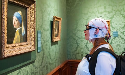 A woman looks at a painting with a brain scanner and eye tracking equipment attached to her head.