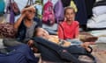 A sleeping baby, flanked by two young girls, is fanned by one of them