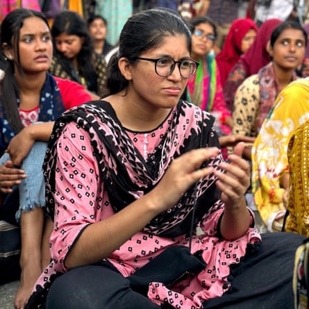 A young woman in spectacles and wearing a kantha scarf sitting at the front of a crowd of women
