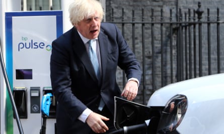 Boris Johnson plugging in an electric car to charge it up while apparently talking to someone off camera