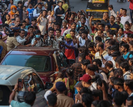 People holding up cameras and phones crowd around two cars