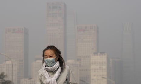A woman wearing a face mask walks past office buildings in Beijing shrouded by pollution haze.