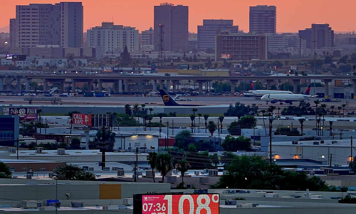 A red neon sign displays an official temperature of 108 degrees F against a backdrop of a Phoenix city skyline at sunset.