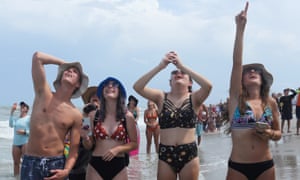 People view the launch of a SpaceX Falcon 9 rocket and Crew Dragon spacecraft from the beach.